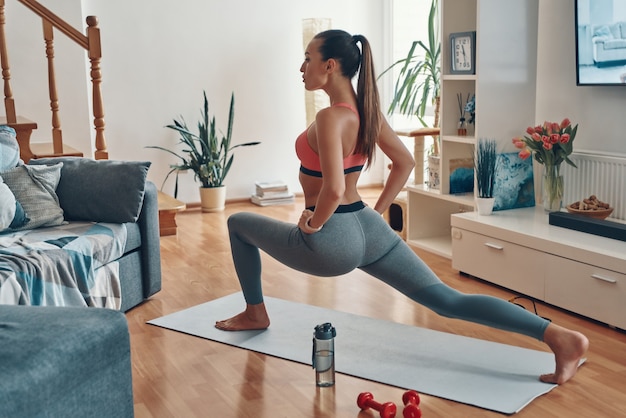 Mujer joven segura de sí misma en ropa deportiva haciendo ejercicio mientras pasa tiempo en casa