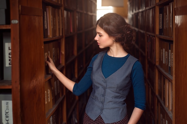 Mujer joven seleccionando el libro del estante de la biblioteca.