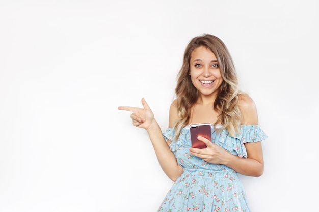 Una mujer joven señala el espacio vacío de la copia de texto o diseño con su dedo sosteniendo un teléfono móvil