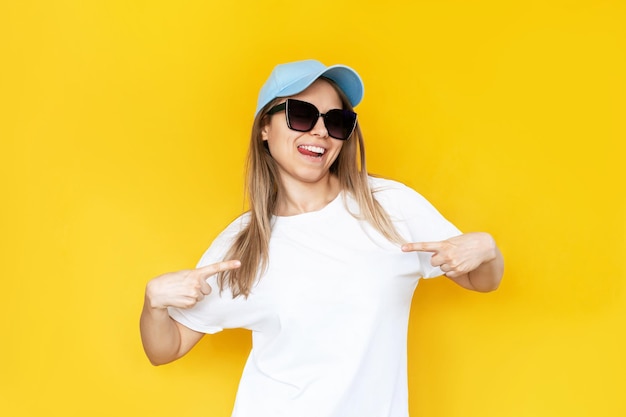 Una mujer joven señalando una camiseta casual blanca con los dedos mostrando un espacio de copia vacío para el diseño