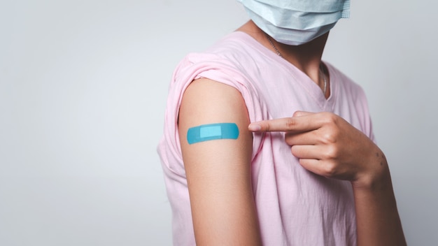 Mujer joven señalando el vendaje adhesivo en su brazo después de la inyección de la vacuna.
