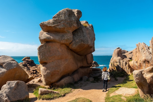 Una mujer joven en un sendero en la costa junto al faro Mean Ruz, puerto de Ploumanach, en la localidad de Perros-Guirec, Cotes-d'Armor, en la Bretaña francesa, Francia.