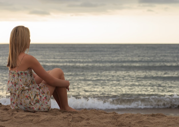 Mujer joven sentada en la arena y mirando al mar.