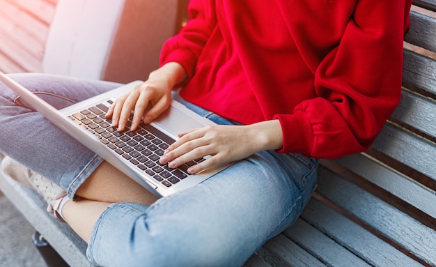 Mujer joven sentada en un banco y escribiendo en la computadora portátil