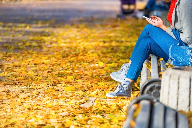 Mujer joven sentada en un banco en el parque de otoño con hojas amarillas caídas