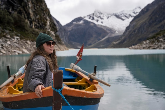 Mujer joven sentada en un bote de madera mientras contempla el paisaje con un lago