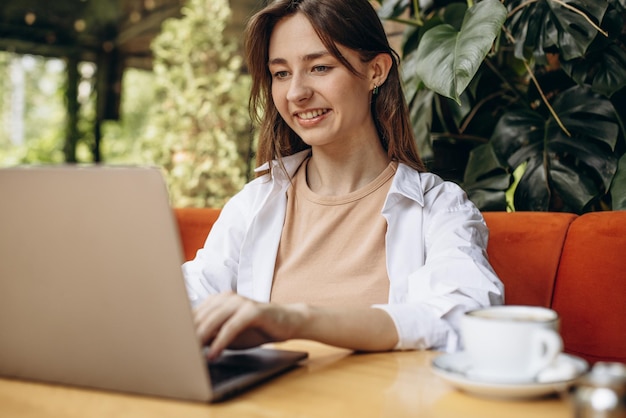 Mujer joven sentada en un café tomando café y trabajando en la computadora