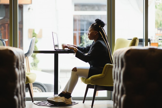 Mujer joven sentada en un café trabajando en un portátil.