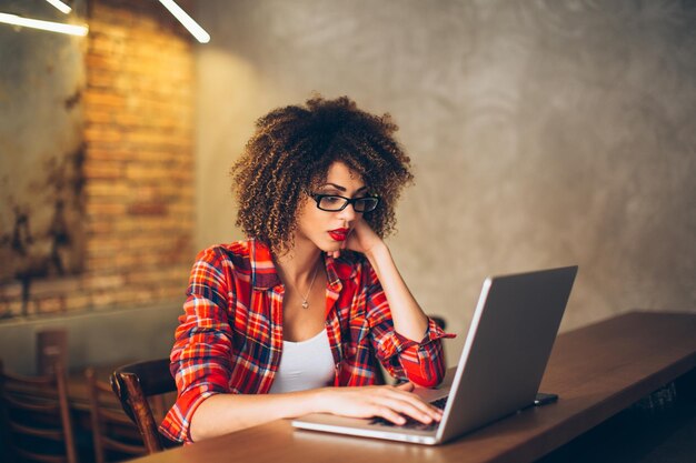 Mujer joven sentada en una cafetería trabajando en una computadora portátil