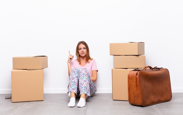 mujer joven sentada entre cajas sintiéndose como un genio sosteniendo el dedo con orgullo en el aire