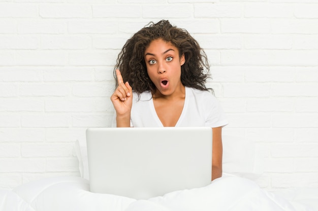 Mujer joven sentada en la cama con el portátil con una gran idea, concepto de creatividad.