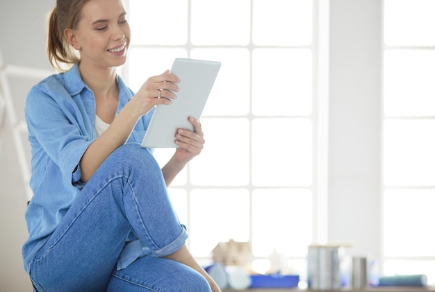 Mujer joven sentada en casa y comprando muebles nuevos a través de Internet usando una tableta