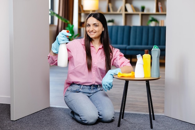 Mujer joven sentada cerca de la mesa con productos de limpieza en casa