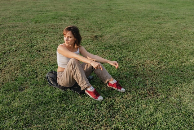 Foto mujer joven sentada en un césped al aire libre durante la hora dorada