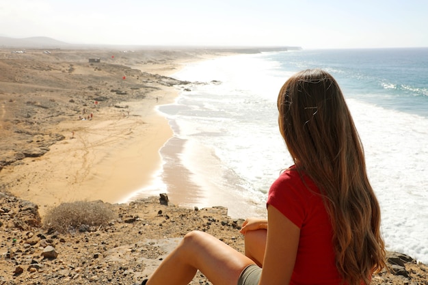 Mujer joven sentada en la cima del acantilado en la costa de Fuerteventura