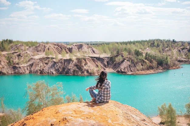 Mujer joven sentada en la cima del montaje y sintiéndose libre y mirando el lago azul