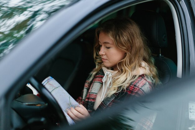 Mujer joven sentada en el coche y sosteniendo el mapa