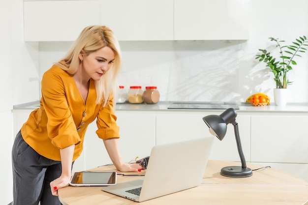 Mujer joven sentada en la cocina y trabajando en equipo portátil.