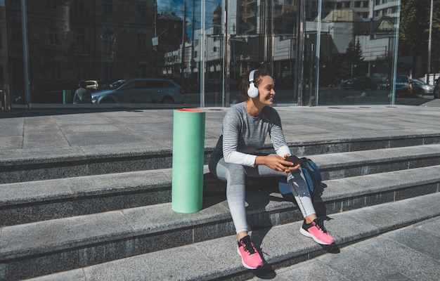 Mujer joven sentada en los escalones escucha música en auriculares