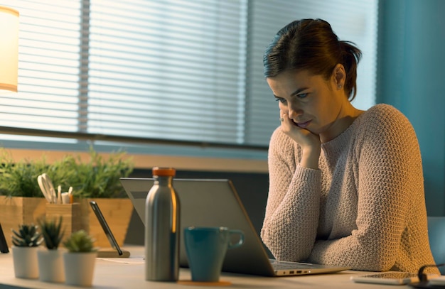 Foto mujer joven sentada en el escritorio y conectándose con su computadora portátil ella está viendo la pantalla