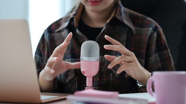 Mujer joven sentada frente a la computadora portátil y grabando haciendo podcast de audio desde un estudio creativo en casa