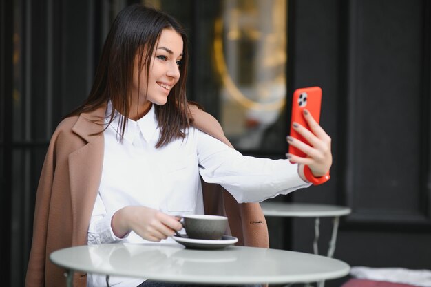 Mujer joven sentada fuera del café con bebida caliente