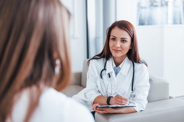 Mujer joven sentada y hablando visita a una doctora en una clínica moderna