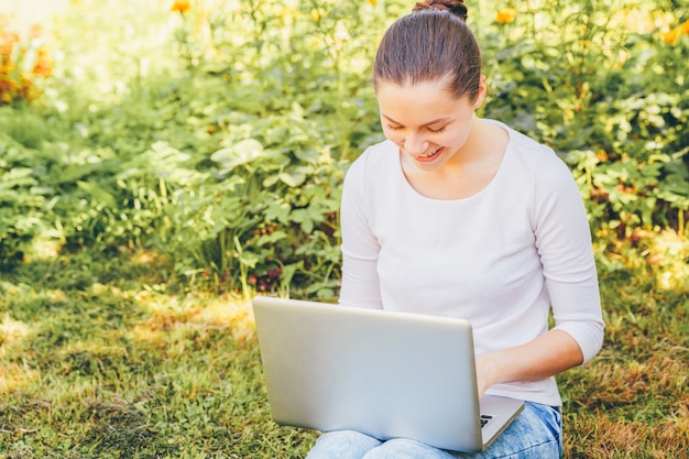 Mujer joven sentada en la hierba verde con su computadora portátil