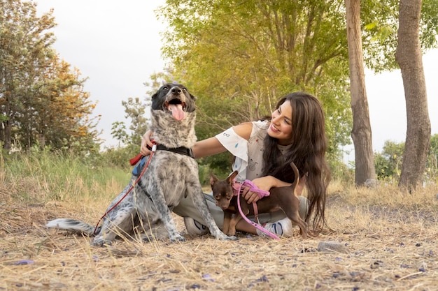 mujer joven sentada jugando con sus perros al aire libre al atardecer concepto petlove