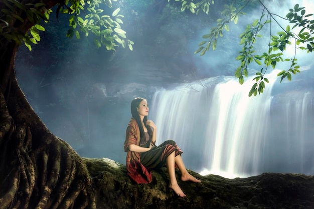 Mujer joven sentada junto a una cascada en el bosque