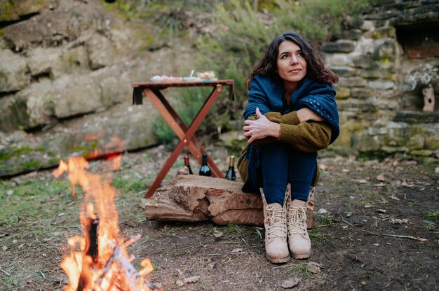 Mujer joven sentada junto a un fuego durante un picnic de invierno.