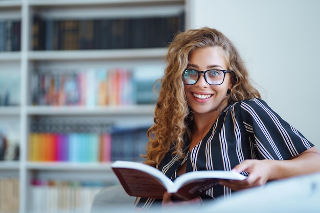 Mujer joven sentada con un libro portátil en la biblioteca y tomando notas de aprendizaje Concepto de educación