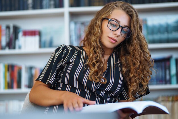 Mujer joven sentada con un libro portátil en la biblioteca y tomando notas de aprendizaje Concepto de educación