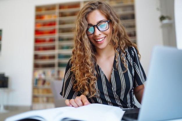 Mujer joven sentada con un libro portátil en la biblioteca y tomando notas de aprendizaje Concepto de educación