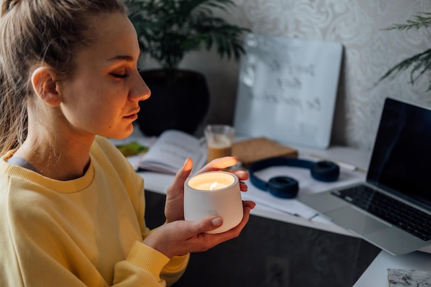 Mujer joven sentada en el lugar de trabajo en la oficina en casa con velas encendidas disfruta de la meditación relajándose en