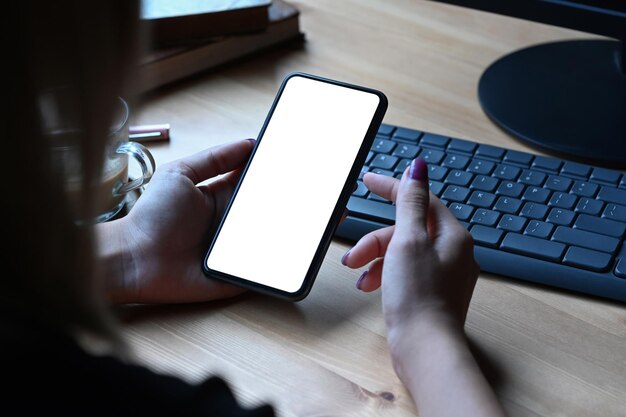 Mujer joven sentada en el lugar de trabajo y usando el teléfono móvil Pantalla vacía para su mensaje de texto o contenido de información