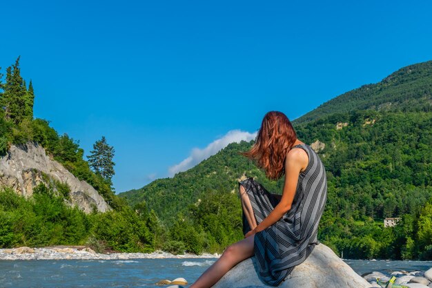 Foto mujer joven sentada en la montaña contra el cielo azul