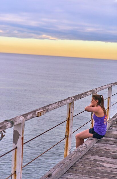 Foto mujer joven sentada en el muelle contra el cielo durante el amanecer