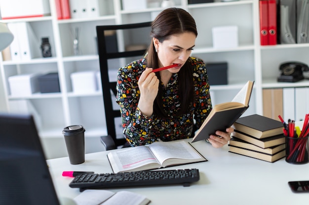 Una mujer joven sentada en la oficina en la computadora Escritorio y trabajando con un libro.