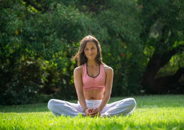 Mujer joven sentada en un parque verde practicando YogaWellness Concept