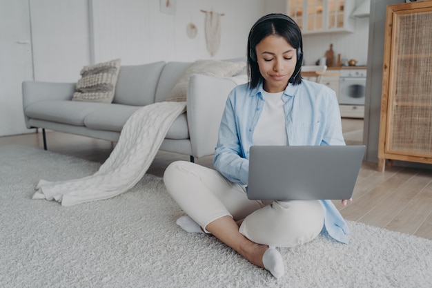 Foto mujer joven está sentada en el piso con video chat en la computadora portátil chica está sonriendo y escribiendo en la pc