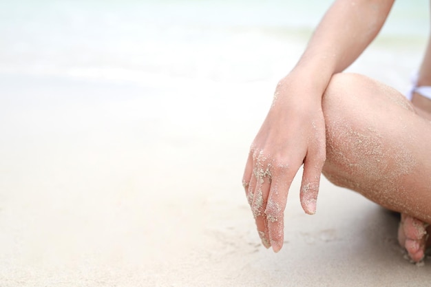 Mujer joven sentada en relajación al aire libre en una playa tropical con partes del cuerpo de arena