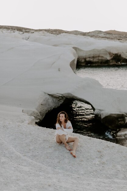 Foto mujer joven sentada en una roca en la playa