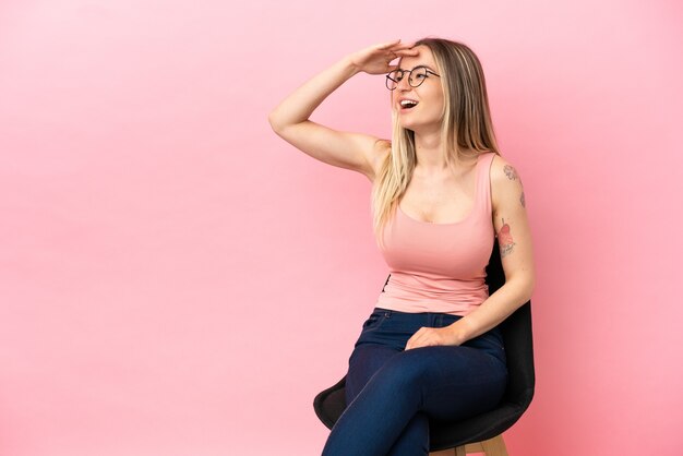 Mujer joven sentada en una silla sobre fondo rosa aislado se ha dado cuenta de algo y tiene la intención de la solución