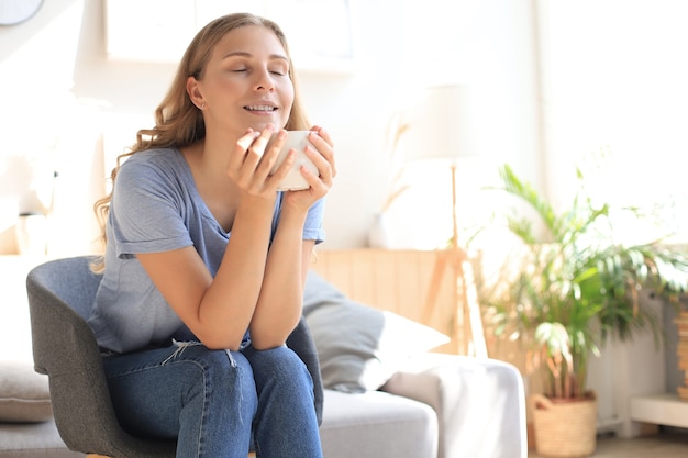 Mujer joven sentada en un sillón y tomando café.