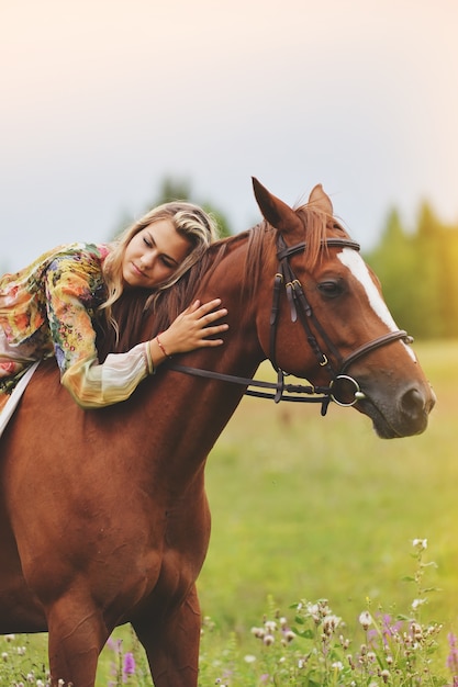 Mujer joven sentada sobre un caballo en una pradera de verano