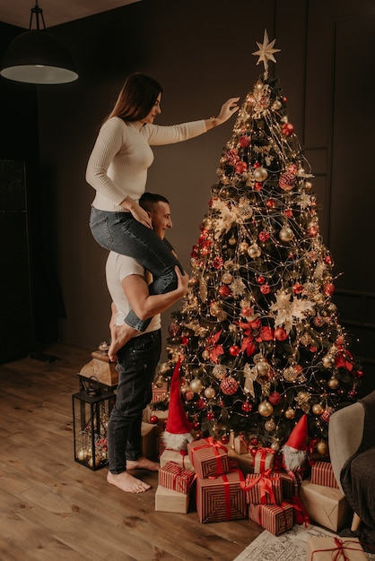 Mujer joven sentada sobre los hombros del hombre y decora un árbol de Navidad