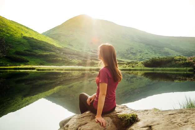 Foto mujer joven sentada sobre una piedra en las montañas en un hermoso lago de montaña al atardecer