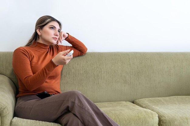 Foto mujer joven sentada en un sofá apuntando un control remoto a un dispositivo electrónico