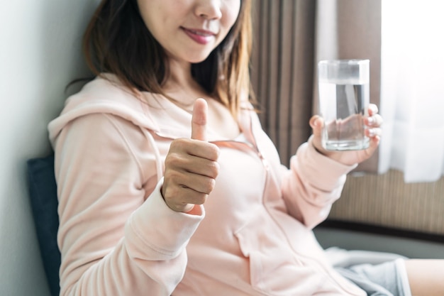 Foto mujer joven sentada en el sofá y beber agua por la mañana